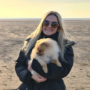Megan stands on a beach holding her pomeranian dog