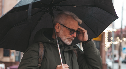 Senior man with a headache with an umbrella in the rain
