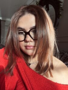 A woman wearing a red top and black glasses with brown hari