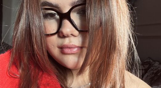 A woman wearing a red top and black glasses with brown hari