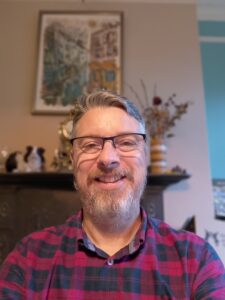 A man with a bear and glasses in a red and black checked shirt