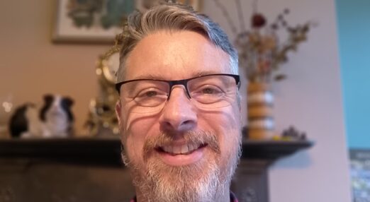 A man with a bear and glasses in a red and black checked shirt