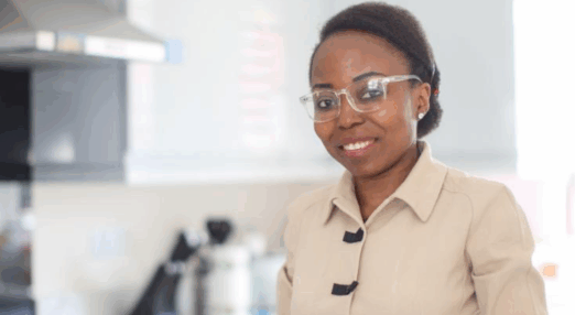 A woman wearing glasses stands beside a laptop