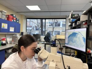 A woman in a white lab coat looks into a microscope