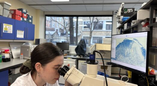 A woman in a white lab coat looks into a microscope