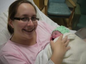 A woman is holding her newborn baby and smiling at the camera.