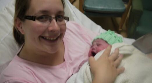 A woman is holding her newborn baby and smiling at the camera.