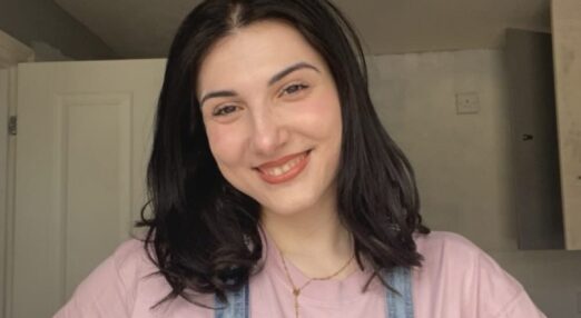 A young woman is standing and smiling at the camera.
