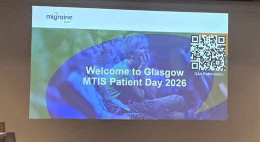 A presentations screen at a conference venue. Banner stands read 'MTIS'.